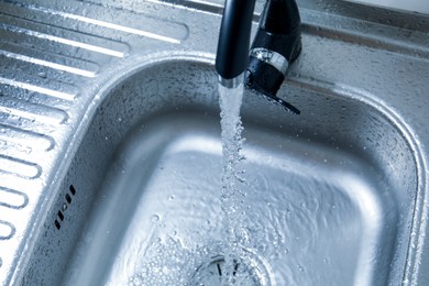 Photo of Water flowing from tap into sink, closeup
