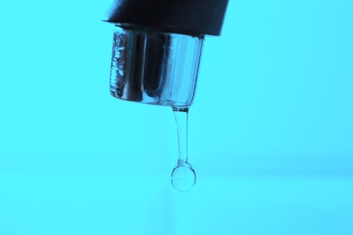 Photo of Water dripping down from faucet on light blue background, closeup