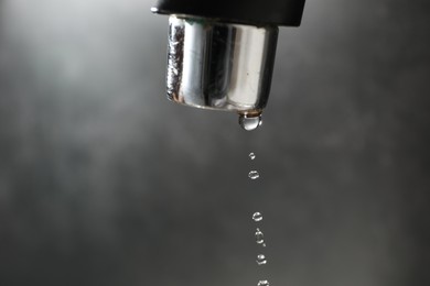 Photo of Water dripping down from faucet on grey background, closeup. Space for text