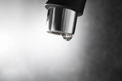 Photo of Water dripping down from faucet on grey background, closeup. Space for text