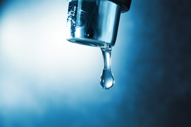 Photo of Water dripping down from faucet on color background, closeup