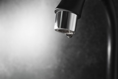 Photo of Water dripping down from faucet on grey background, closeup. Space for text