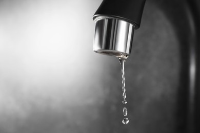 Photo of Water dripping down from faucet on grey background, closeup. Space for text
