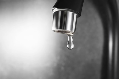 Photo of Water dripping down from faucet on grey background, closeup. Space for text