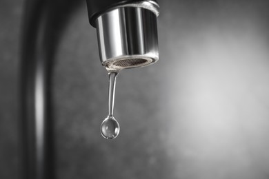 Photo of Water dripping down from faucet on grey background, closeup. Space for text