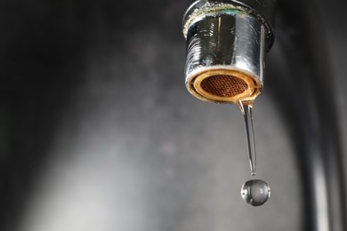 Photo of Water dripping down from faucet on grey background, closeup. Space for text