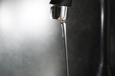 Photo of Water dripping down from faucet on grey background, closeup. Space for text