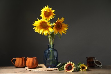 Photo of Beautiful sunflowers in vase, candle and cups on wooden table against black background