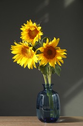 Photo of Beautiful sunflowers in vase on wooden table against black background