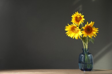 Photo of Beautiful sunflowers in vase on wooden table against black background, space for text