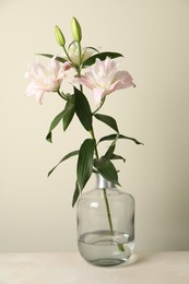 Photo of Beautiful lily flowers in glass vase on table near beige wall