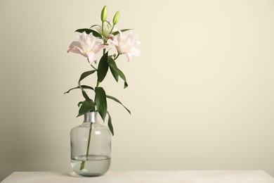 Photo of Beautiful lily flowers in glass vase on table near beige wall, space for text