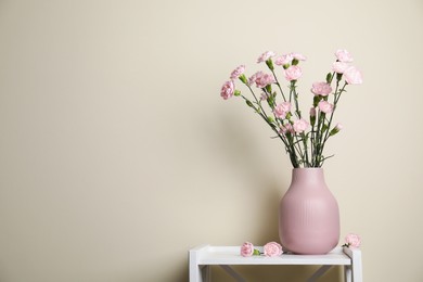 Photo of Beautiful carnation flowers in vase on white stand near beige wall indoors, space for text