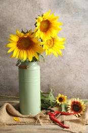 Photo of Beautiful sunflowers in can used as vase and secateurs on wooden table