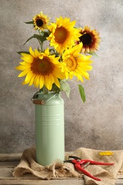 Photo of Beautiful sunflowers in can used as vase and secateurs on wooden table