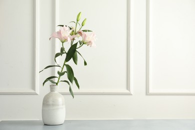 Photo of Beautiful lily flowers in vase on grey table near white wall, space for text