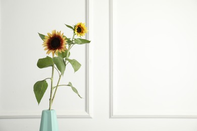 Photo of Beautiful sunflowers in vase near white wall indoors, space for text