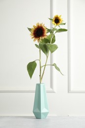 Photo of Beautiful sunflowers in vase on grey table near white wall indoors
