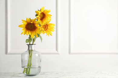 Photo of Beautiful sunflowers in glass vase on white marble table indoors, space for text