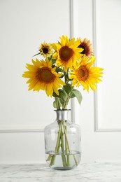 Photo of Beautiful sunflowers in glass vase on white marble table indoors
