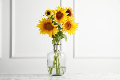 Photo of Beautiful sunflowers in glass vase on white marble table indoors