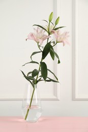 Photo of Beautiful lily flowers in glass vase on pink wooden table near white wall indoors