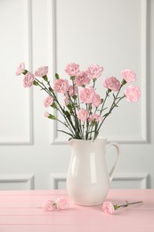 Photo of Beautiful carnation flowers in vase on pink wooden table near white wall indoors