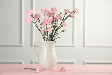 Photo of Beautiful carnation flowers in vase on pink wooden table near white wall indoors, space for text