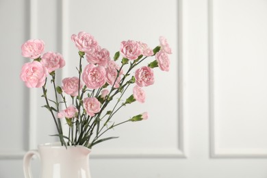 Photo of Beautiful carnation flowers in vase near white wall, closeup. Space for text