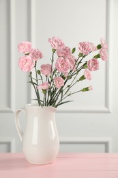 Photo of Beautiful carnation flowers in vase on pink wooden table near white wall indoors