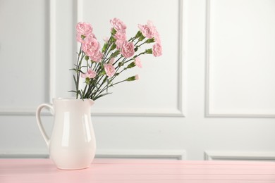 Photo of Beautiful carnation flowers in vase on pink wooden table near white wall indoors, space for text