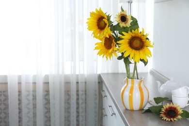 Photo of Beautiful sunflowers in jug on wooden cabinet indoors, space for text