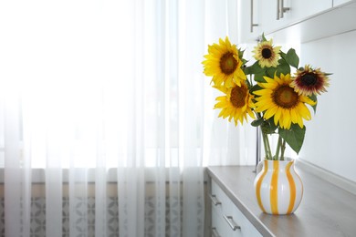 Photo of Beautiful sunflowers in jug on wooden cabinet indoors, space for text
