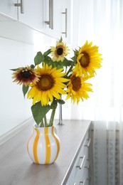 Photo of Beautiful sunflowers in jug on wooden cabinet indoors