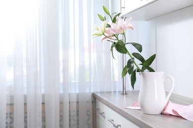 Photo of Beautiful lily flowers in jug on wooden cabinet indoors, space for text