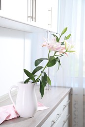 Photo of Beautiful lily flowers in jug on wooden cabinet indoors