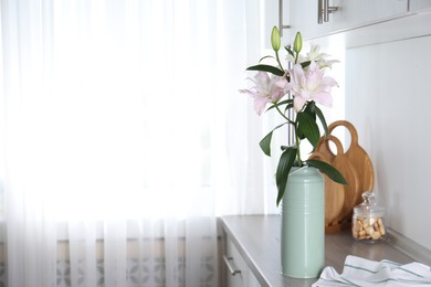 Photo of Beautiful lily flowers in can used as vase on wooden cabinet indoors, space for text