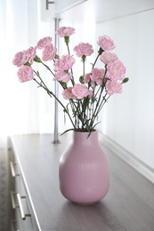 Photo of Beautiful carnation flowers in vase on wooden cabinet indoors