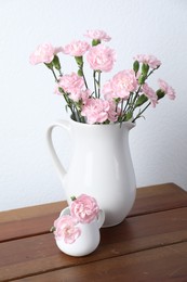 Photo of Beautiful carnation flowers in jugs on wooden table near white wall indoors