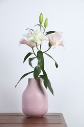 Photo of Beautiful lily flowers in vase on wooden table near white wall indoors