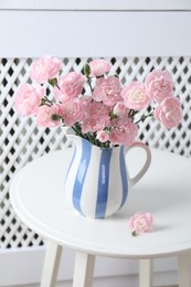 Photo of Beautiful carnation flowers in jug on white table indoors