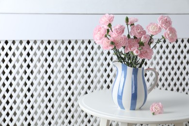 Photo of Beautiful carnation flowers in jug on white table indoors, space for text