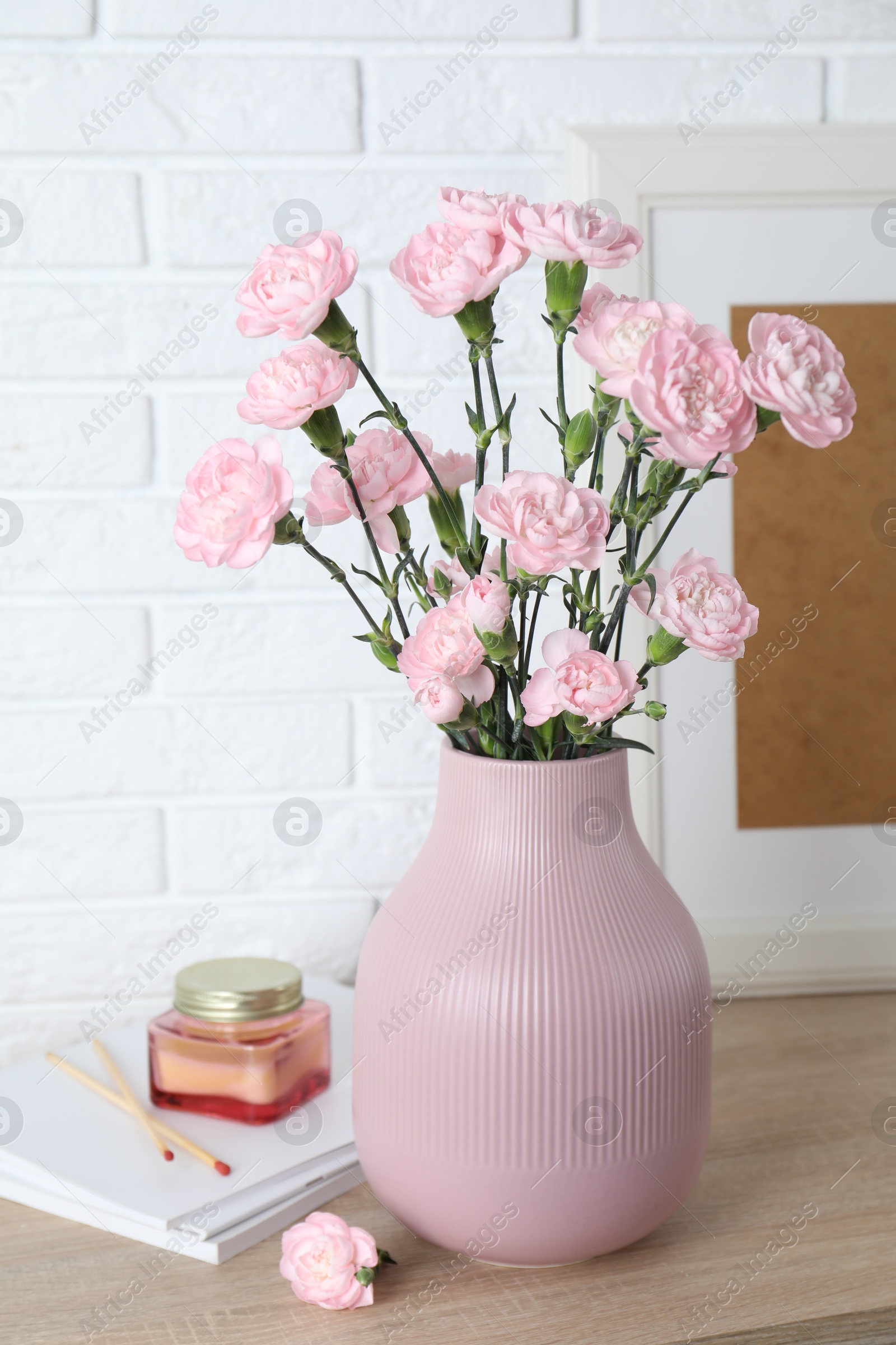 Beautiful carnation flowers in vase and other decor on wooden cabinet near white brick wall indoors Photo of Beautiful carnation flowers in vase and other decor on wooden cabinet near white brick wall indoors