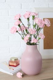 Photo of Beautiful carnation flowers in vase and other decor on wooden cabinet near white brick wall indoors