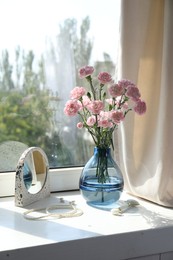 Photo of Beautiful carnation flowers in vase, mirror, jewellery and face roller near window indoors