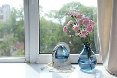 Photo of Beautiful carnation flowers in vase, mirror, jewellery and face roller near window indoors