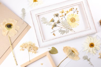 Photo of Beautiful dry flowers, green leaves and picture frame elements on white background, flat lay