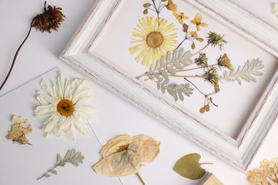 Photo of Beautiful dry flowers, green leaves, picture frame and glass on white background, flat lay