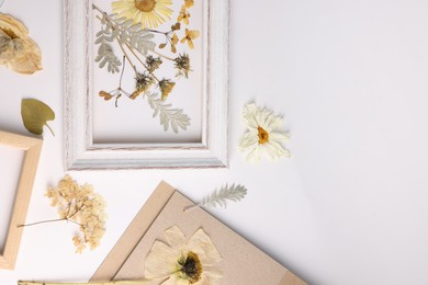 Photo of Beautiful dry flowers, green leaves and picture frame on white background, flat lay. Space for text