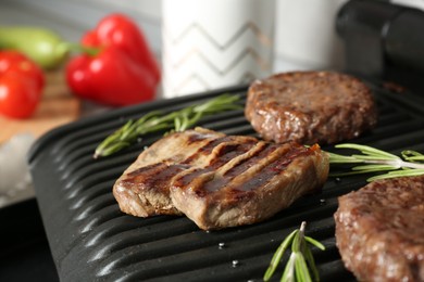 Photo of Open electric grill with beef steak, cutlets and rosemary on table, closeup